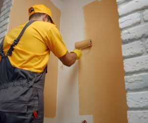 Worker painting wall with paint roller.